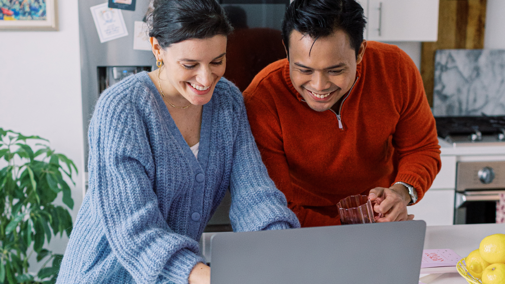 Woman and man smile at a laptop, excited to plan their wedding