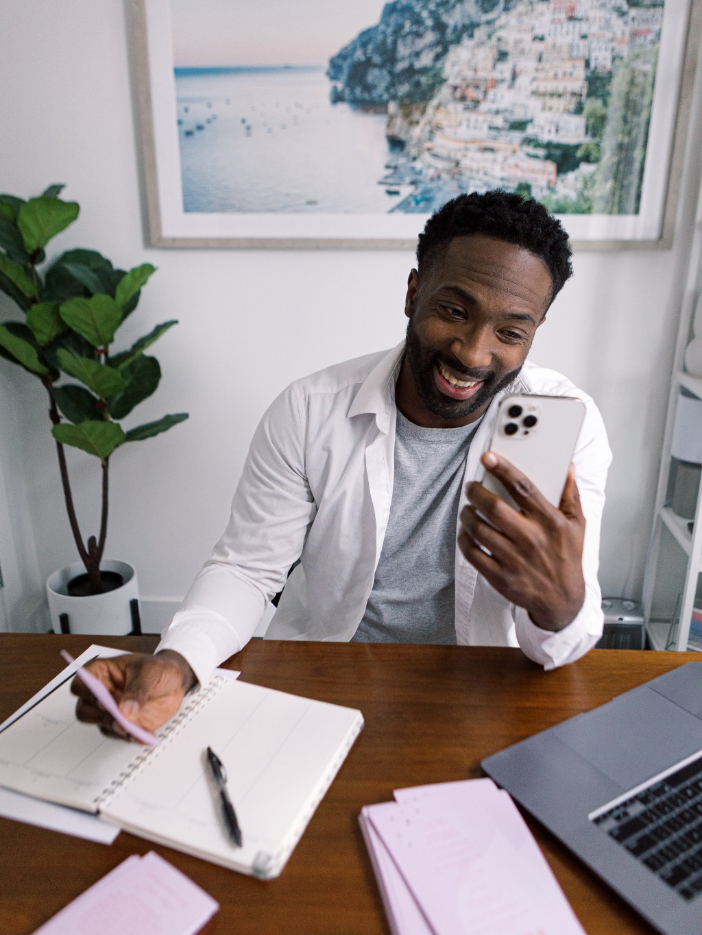 Man on phone smiling holding a pen over a notebook