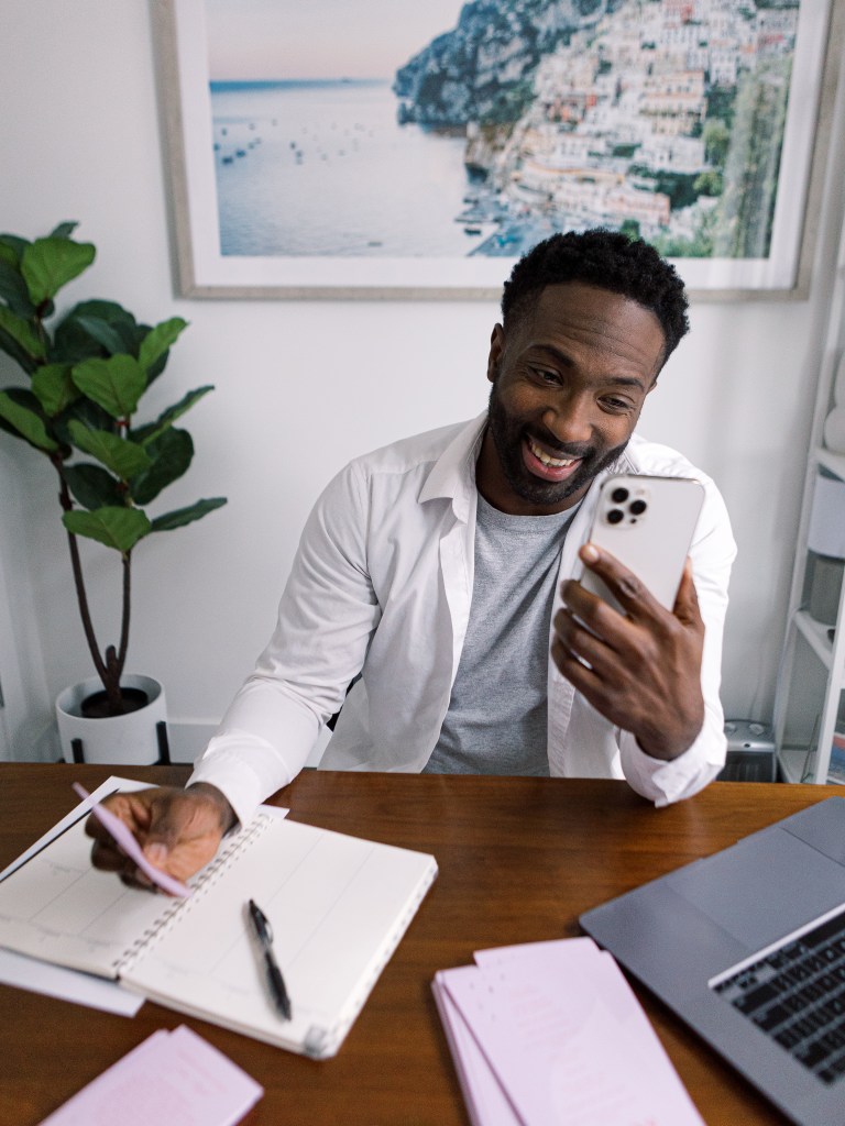 Man on phone smiling holding a pen over a notebook