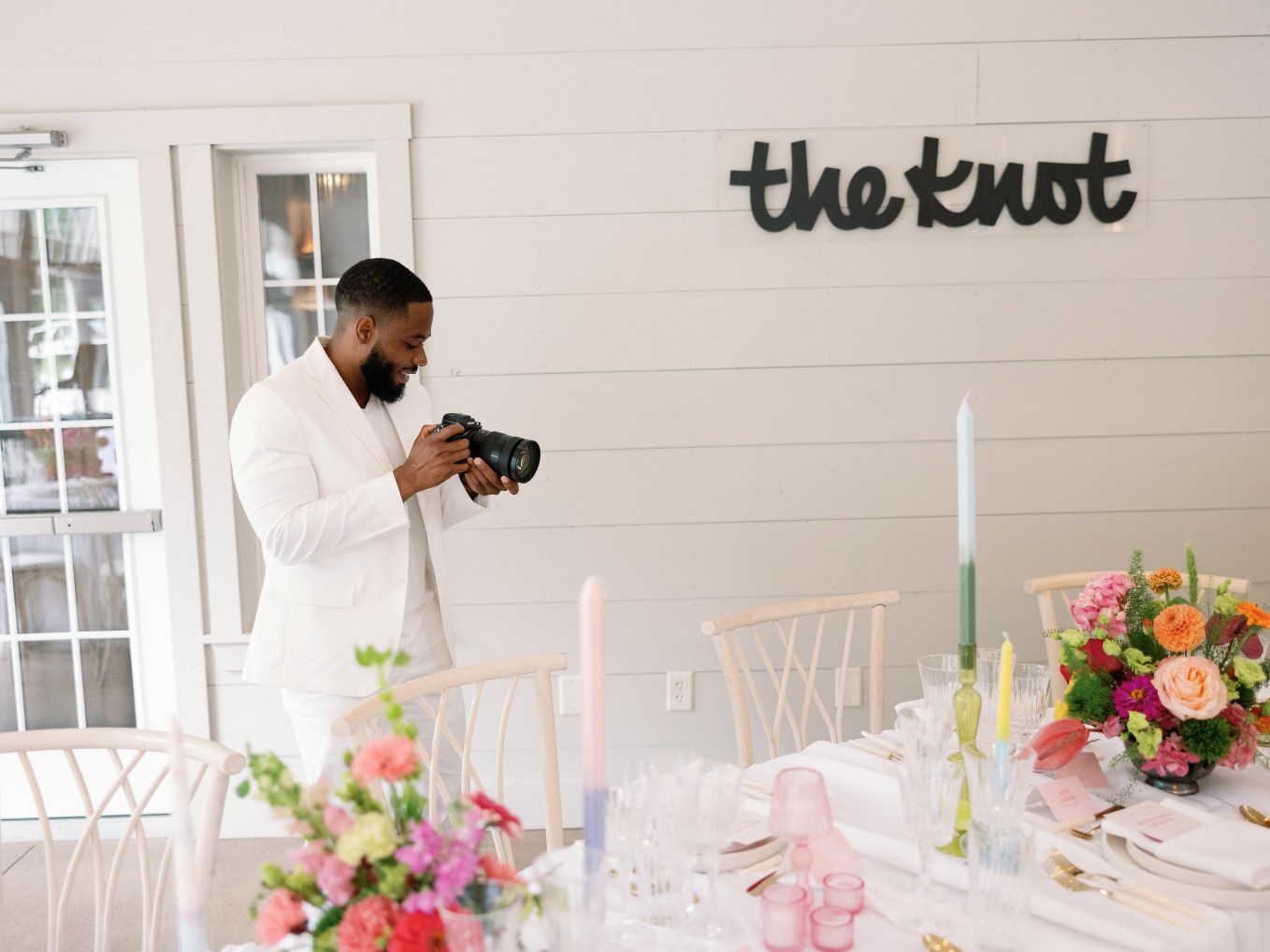 Man holding a camera at a wedding with The Knot logo behind him.